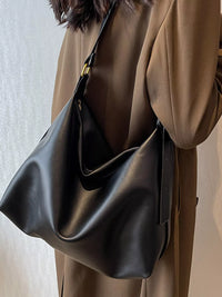 Person wearing a brown coat holding a black leather handbag against a neutral background