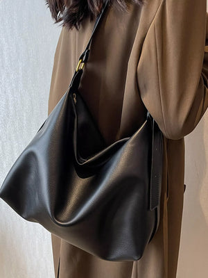 Person wearing a brown coat holding a black leather handbag against a neutral background