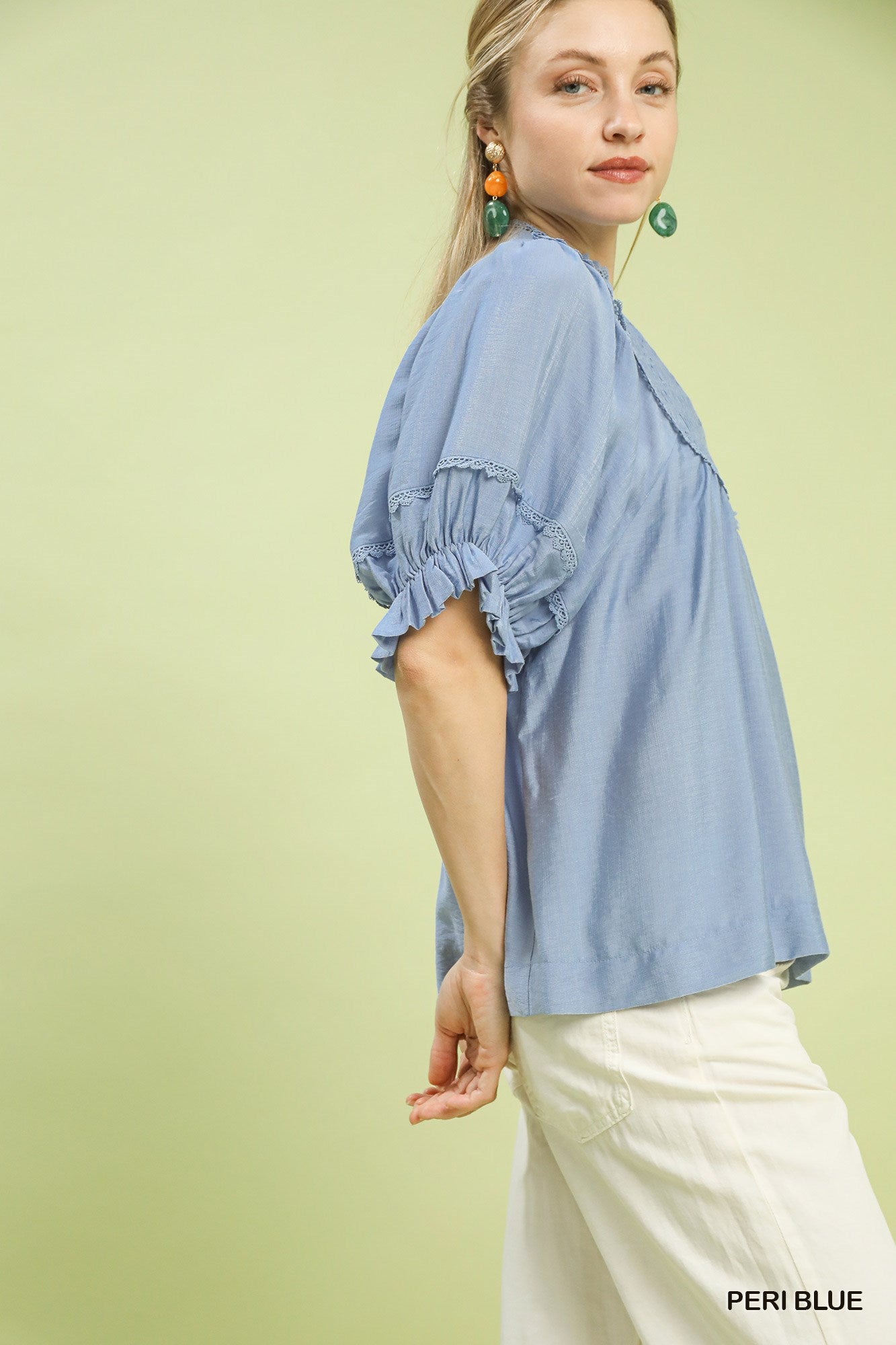 Woman wearing a light blue blouse with ruffled sleeves on a light green background