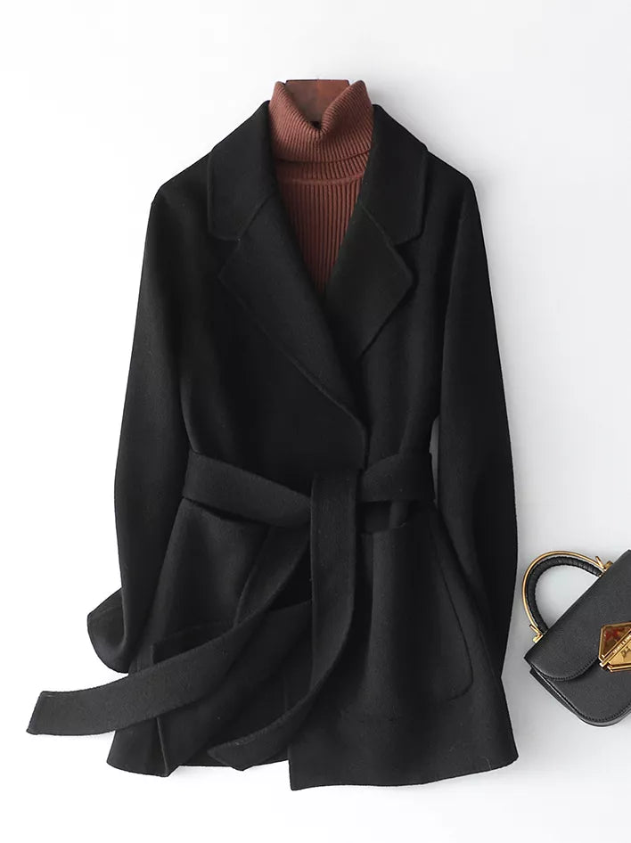 A black belted wrap coat styled over a brown ribbed turtleneck sweater, displayed on a white background next to a black handbag.