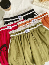 Four pairs of shorts in different colors with lace trim on a white surface.