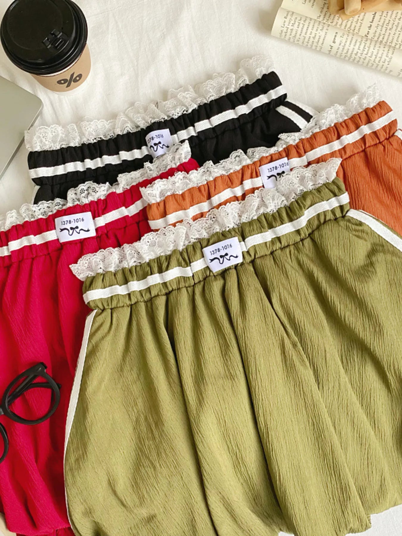 Four pairs of shorts in different colors with lace trim on a white surface.
