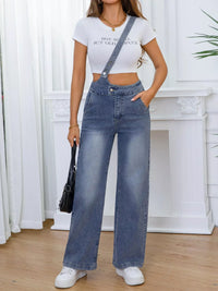 Person wearing a white crop top and blue denim overalls standing indoors.