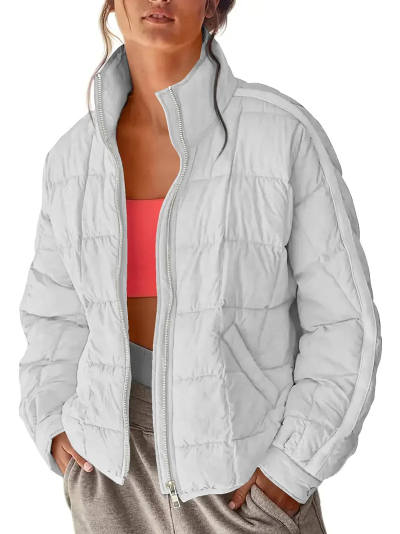 Person wearing a light gray quilted jacket over a pink sports bra and beige pants on a white background