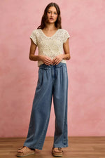 Woman wearing a white lace top and blue jeans against a pink background