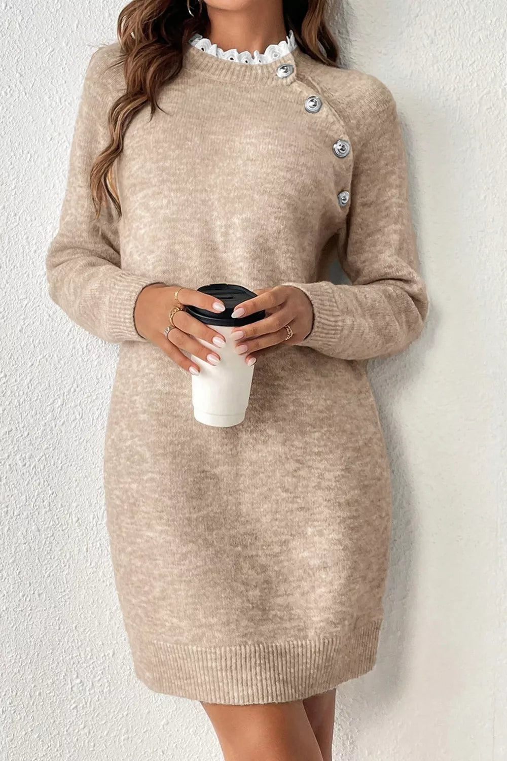 Beige sweater dress worn by a person holding a white cup against a white background