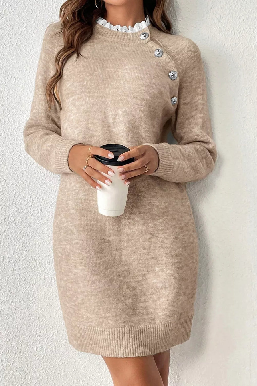 Beige sweater dress worn by a person holding a white cup against a white background