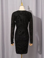 A black long-sleeve bodycon dress with floral lace applique and ruching, displayed on a mannequin against a light gray curtain backdrop.