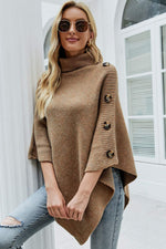 Woman wearing a brown poncho with buttons, standing in front of a white building.