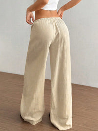 Beige wide-leg pants worn by a person on a wooden floor with a white wall background