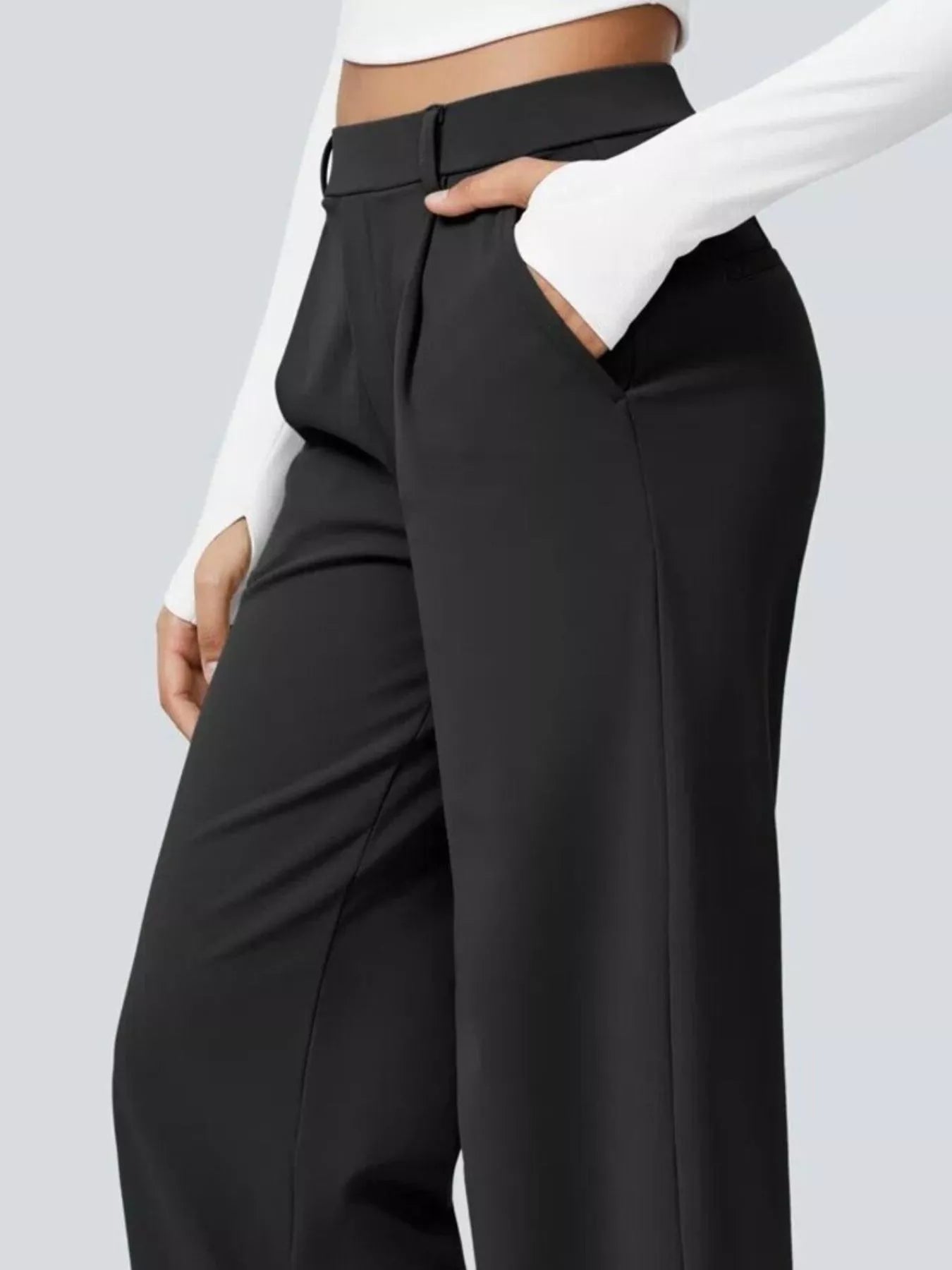 Black high-waisted pants worn with a white long-sleeve top on a light gray background