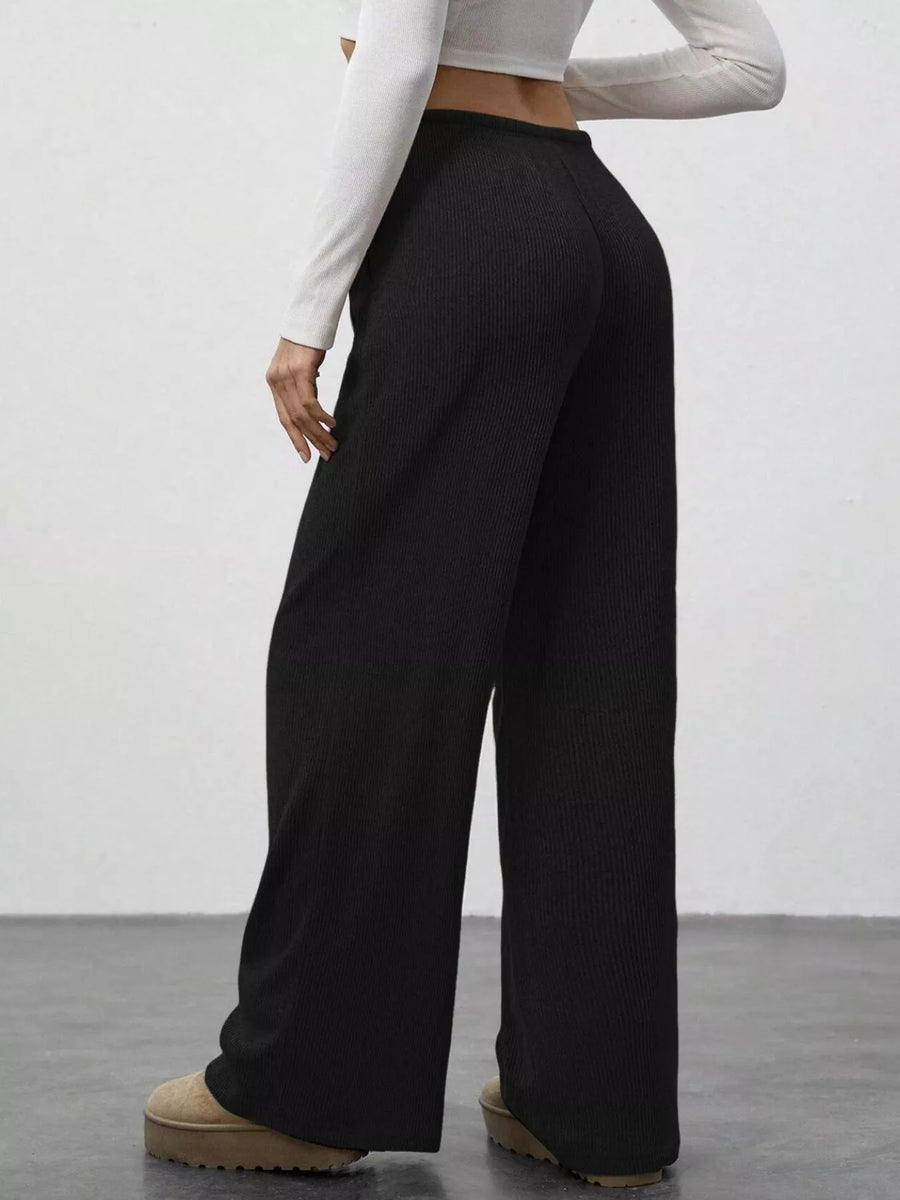 Person wearing black wide-leg pants and a white long-sleeve top against a plain background