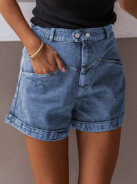 Person wearing blue denim shorts with a neutral background