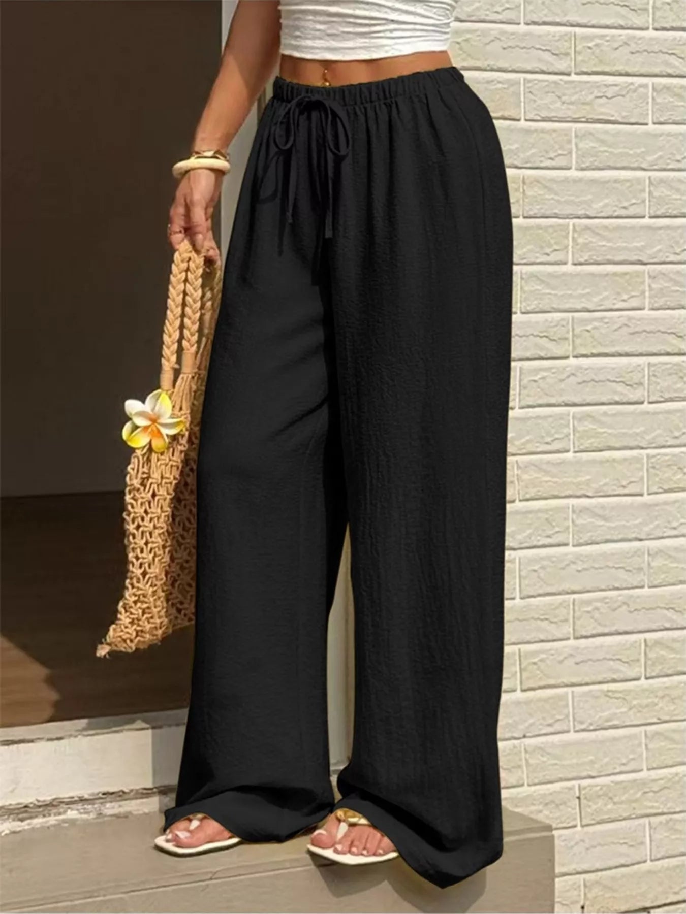 Person wearing black wide-leg pants standing against a brick wall.