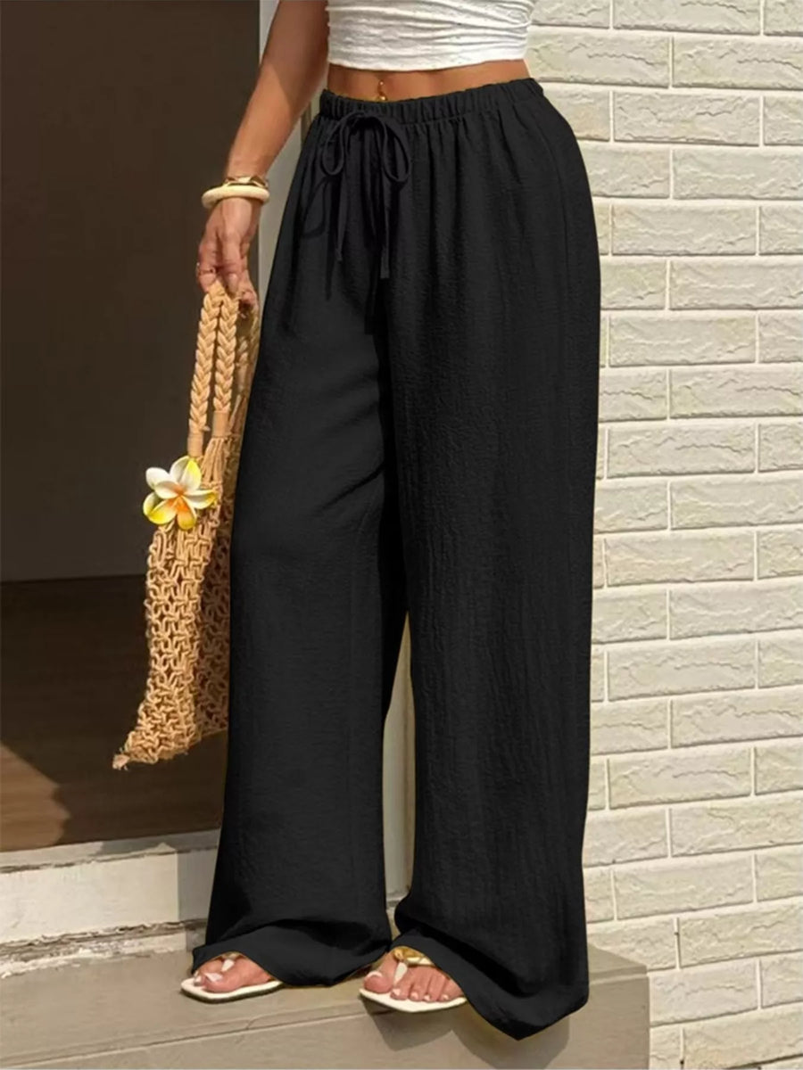 Person wearing black wide-leg pants standing against a brick wall.