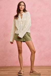 Woman wearing a white lace top and green shorts against a pink background