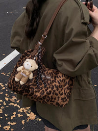 Person holding a leopard print handbag with a teddy bear charm on a street.