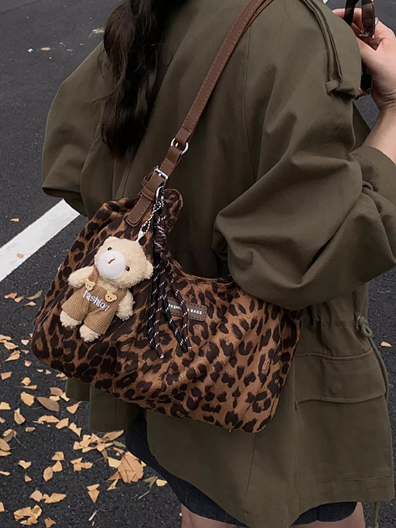 Person holding a leopard print handbag with a teddy bear charm on a street.