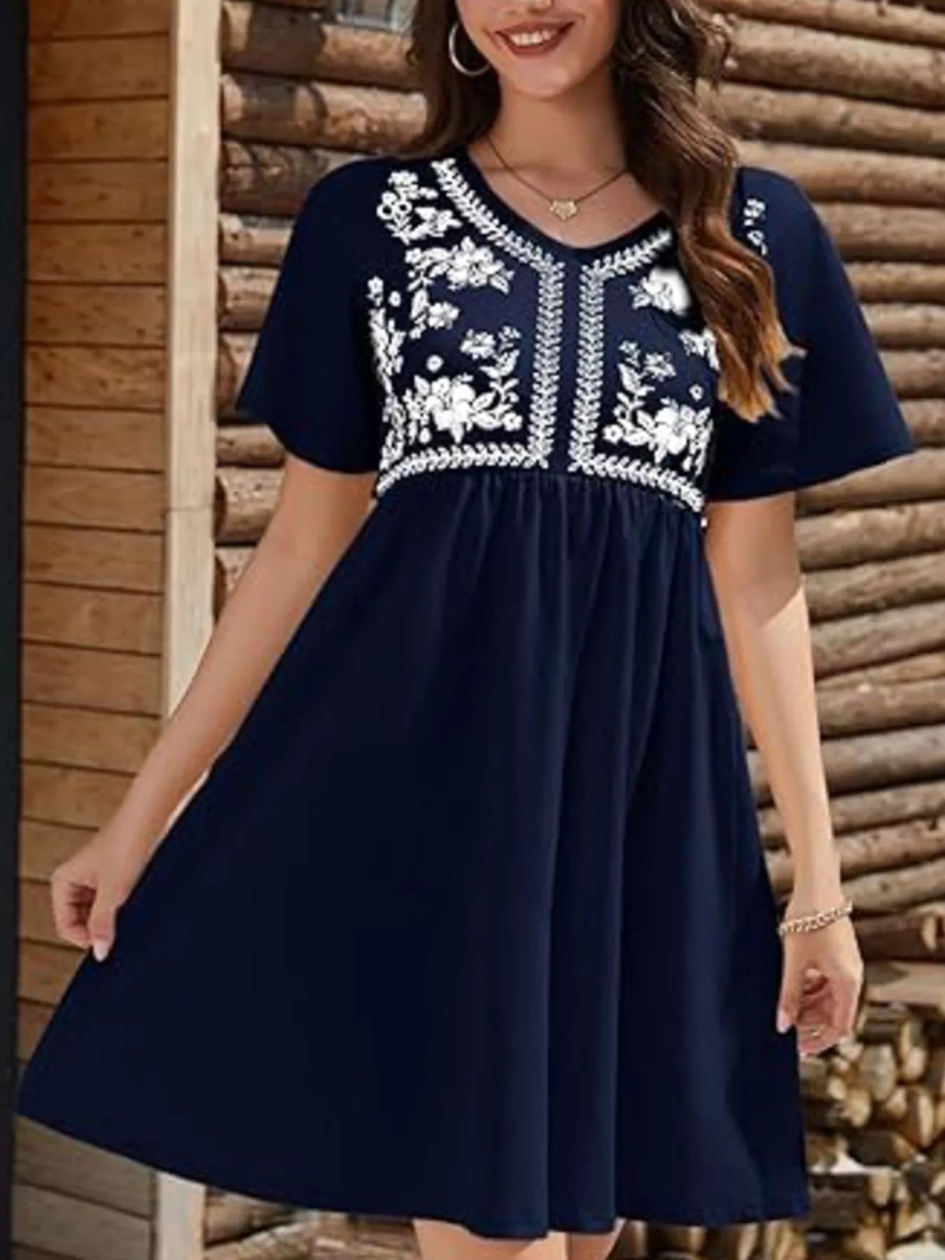 Woman wearing a navy blue dress with white floral embroidery against a wooden background