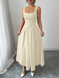 Woman wearing a beige sleeveless dress standing in a room with white curtains.