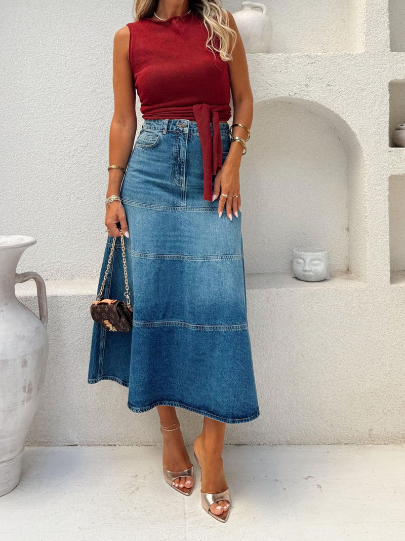 Woman wearing a red top and blue denim skirt standing in a minimalistic indoor setting.