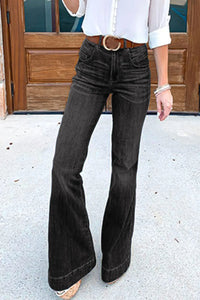 Person wearing black flared jeans and a white shirt in front of a wooden door.