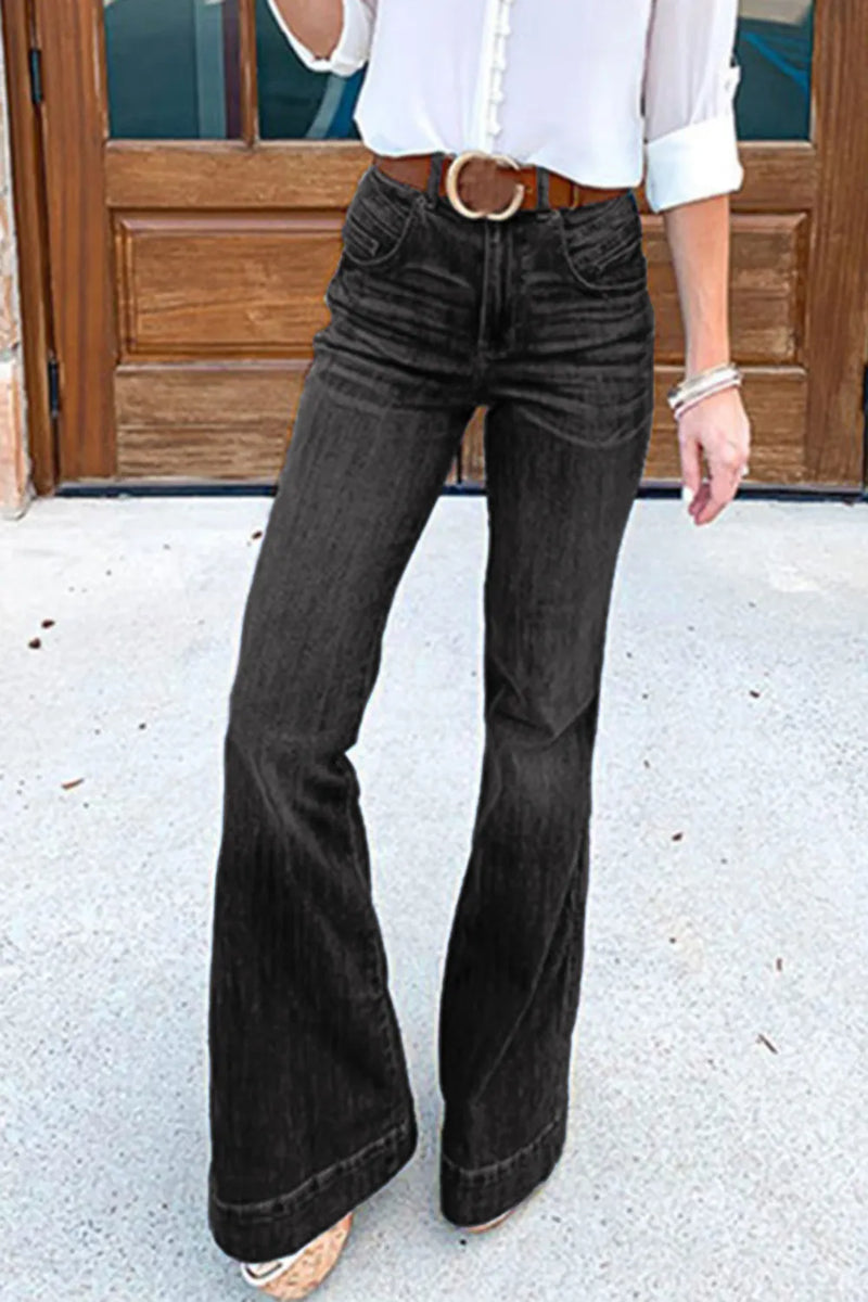 Person wearing black flared jeans and a white shirt in front of a wooden door.