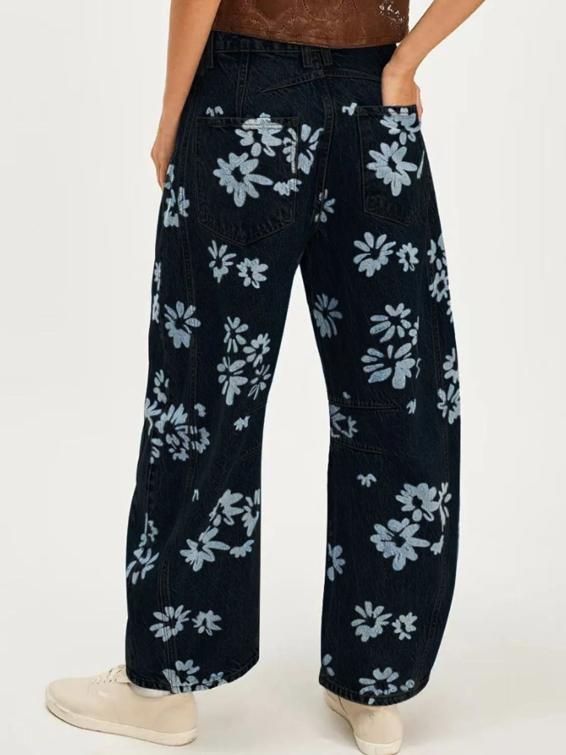 Navy blue jeans with white floral patterns worn by a person on a white background