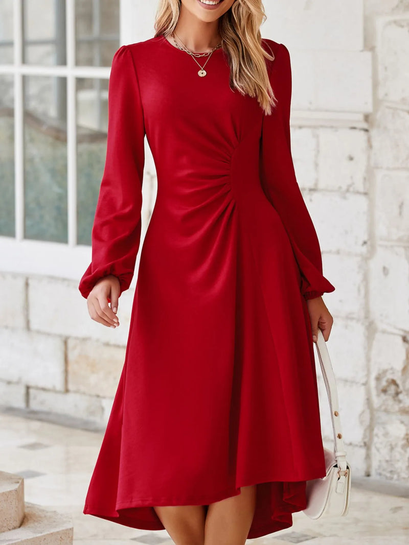 Woman wearing a red dress with long sleeves against a white brick wall.