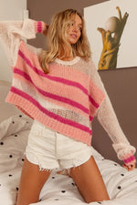 Woman wearing a pink and white striped sweater and white shorts, standing in a room with a painting on the wall.