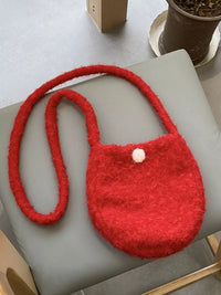 Red textured handbag with a white pom-pom on a light gray surface.