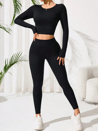 Person wearing a black long-sleeve top and leggings set with white sneakers, standing against a white curtain background.