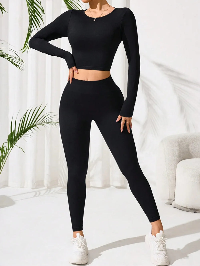 Person wearing a black long-sleeve top and leggings set with white sneakers, standing against a white curtain background.