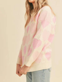Person wearing a pink and beige sweater with heart pattern on a beige background