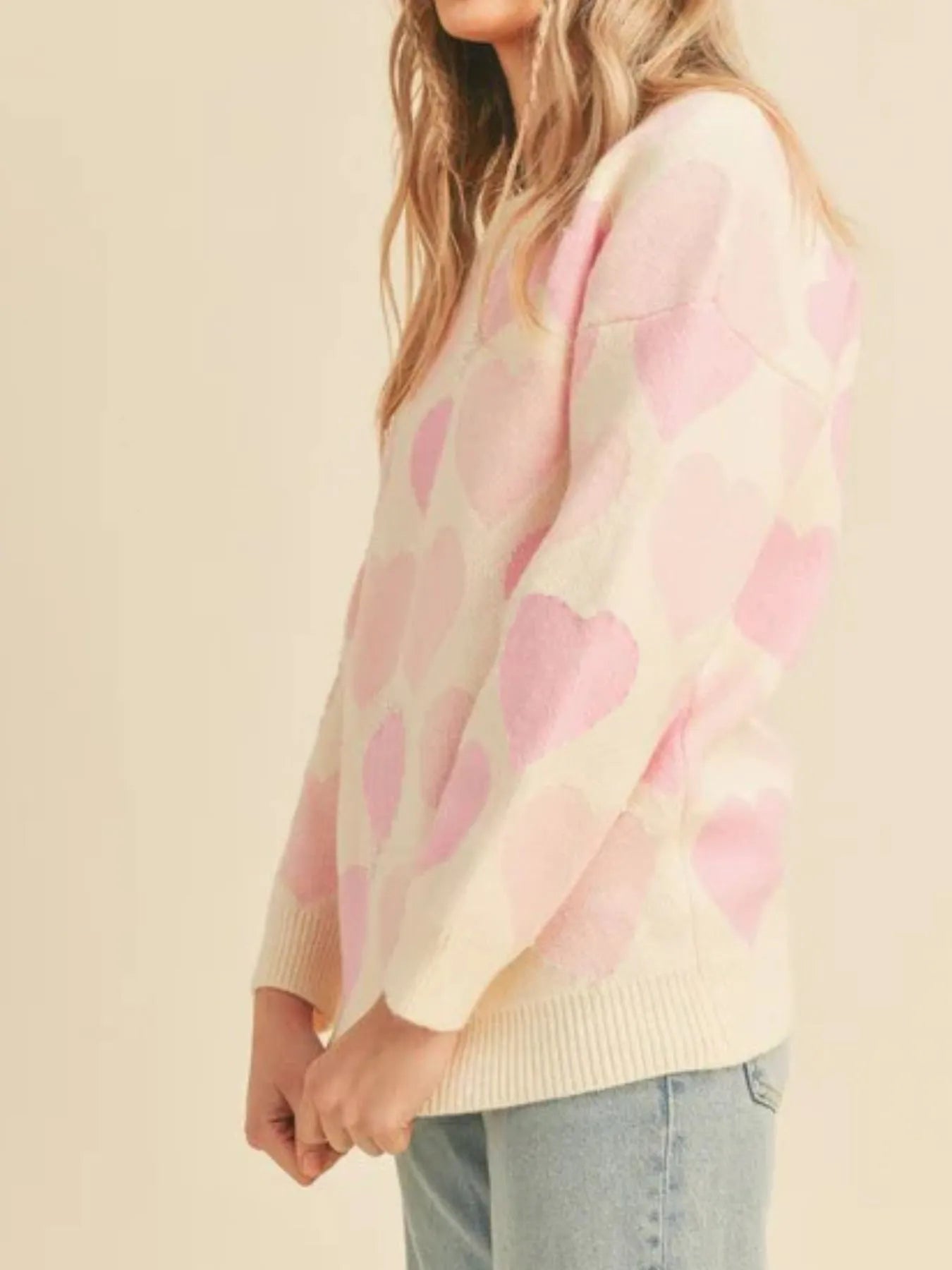 Person wearing a pink and beige sweater with heart pattern on a beige background