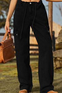Person wearing black cargo pants holding a brown leather bag outdoors.