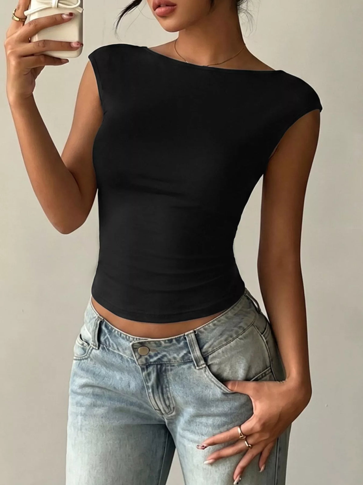 Person wearing a black top and light blue jeans against a neutral background