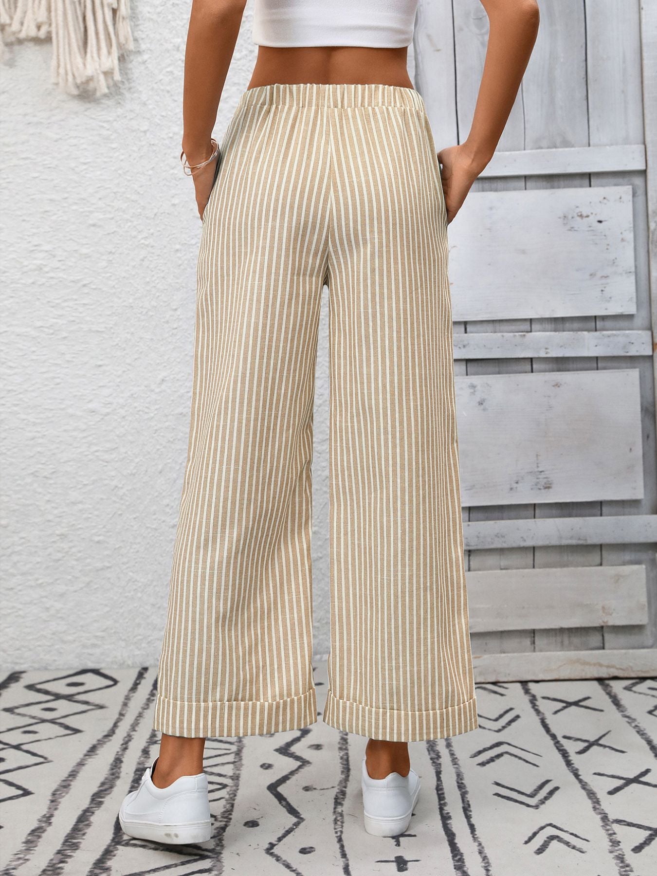 Person wearing beige striped wide-leg pants with a white top against a light wooden panel background.