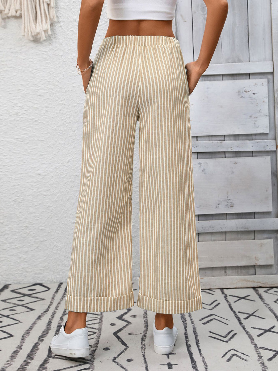 Person wearing beige striped wide-leg pants with a white top against a light wooden panel background.