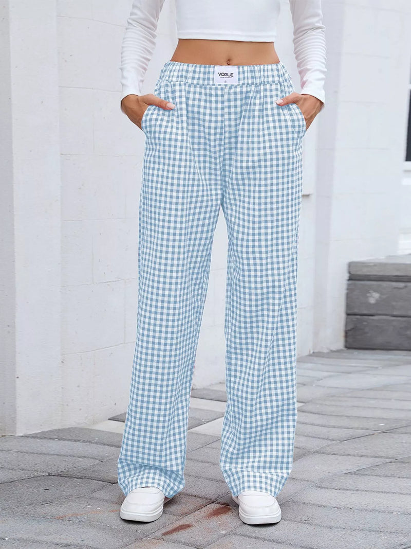 Person wearing light blue and white checkered pants with a white top and shoes on a gray pavement.