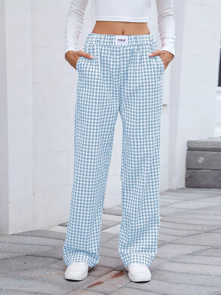 Person wearing light blue and white checkered pants with a white top and shoes on a gray pavement.