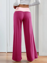 Person wearing pink wide-leg pants and a white long-sleeve top on a wooden floor.