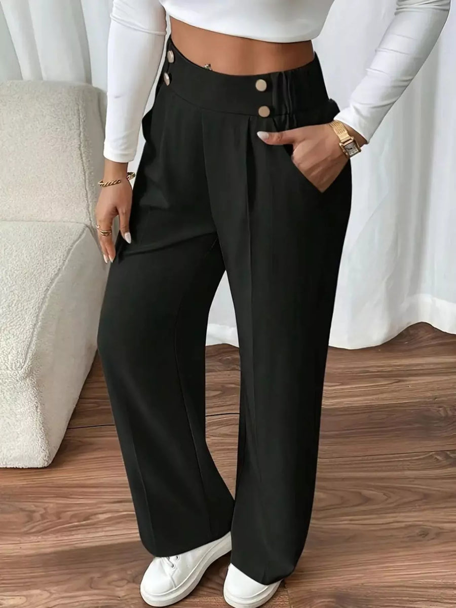 Person wearing black wide-leg pants with a white top and white sneakers on a wooden floor.