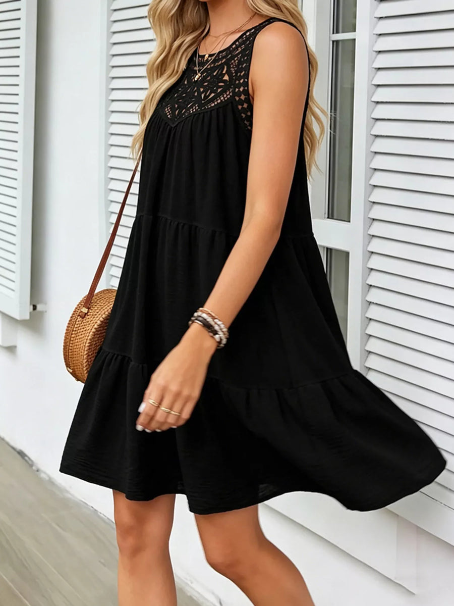 Woman wearing a black dress with lace details in front of a white building.