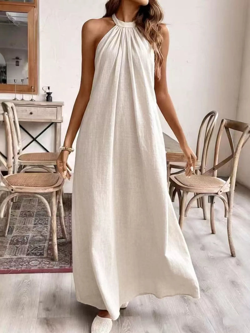 Woman wearing a white halter neck dress in a room with wooden chairs and a mirror.