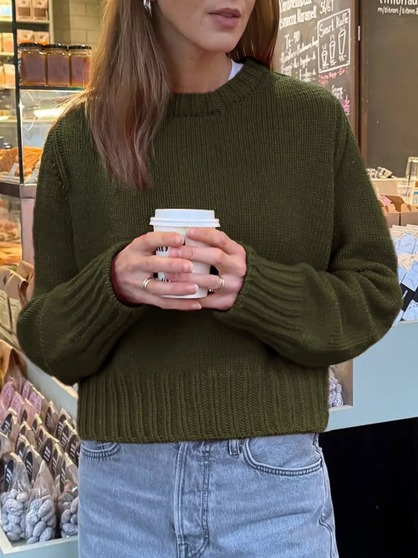 Person wearing a green sweater holding a coffee cup in a store setting