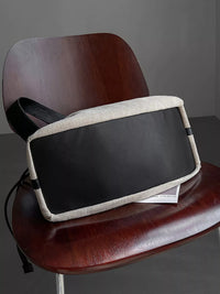 Black and beige bag on a wooden chair against a gray background
