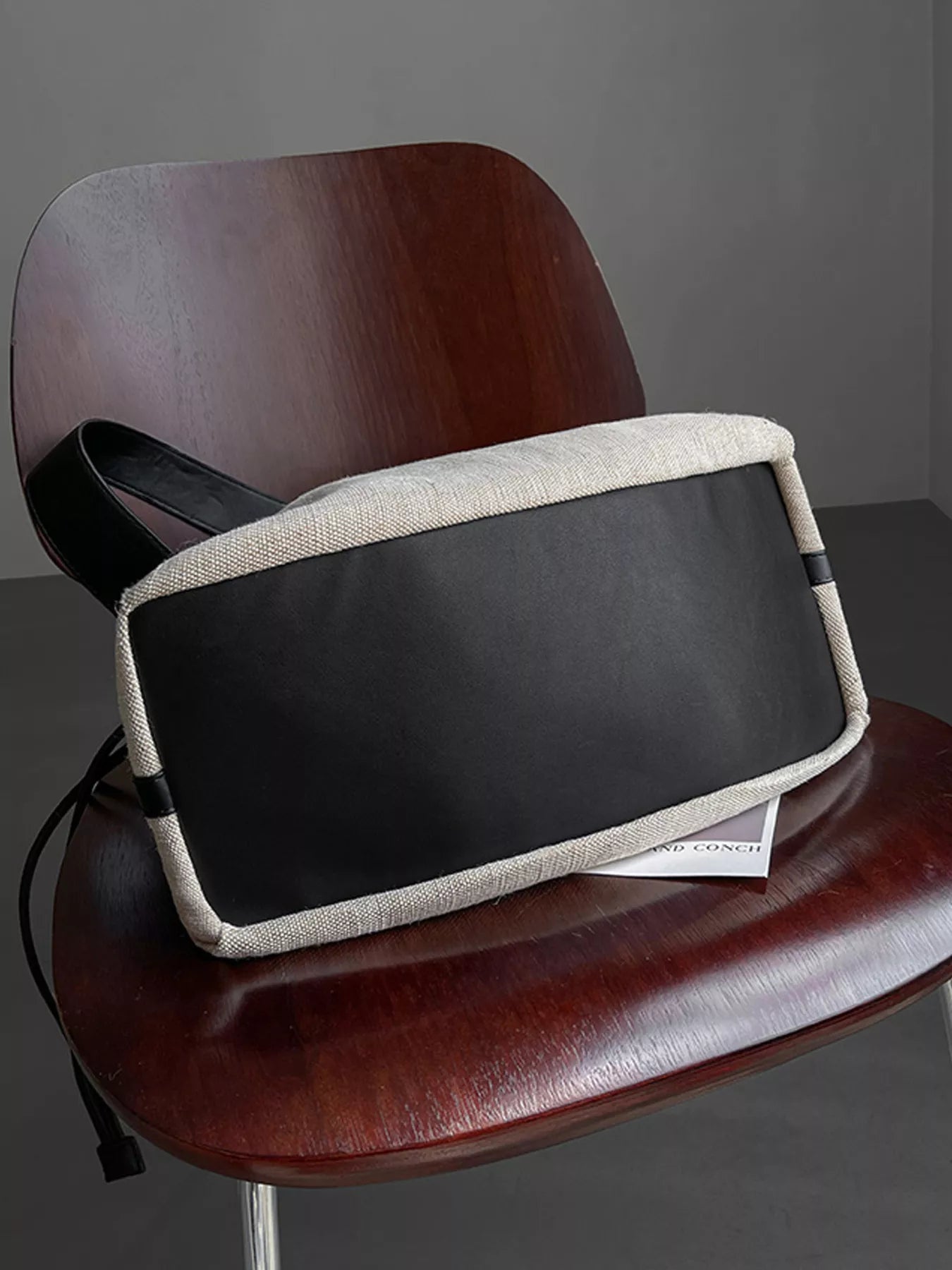 Black and beige bag on a wooden chair against a gray background