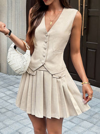 Woman wearing a beige sleeveless dress with a pleated skirt, holding a white handbag.