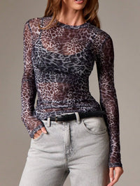 Person wearing a sheer leopard print top and light jeans on a neutral background
